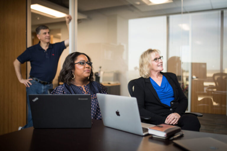 Two women and a man meeting in a glass office with laptops